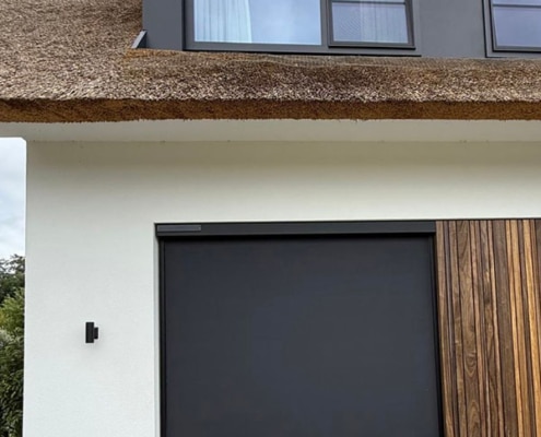 somfy-solar-windvast-screen Close-up van het mat zwarte doek van een Heroal solar screen, passend bij de zwarte kozijnen en houten details van de woning.
