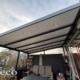 Zonwerende plissé onder een aluminium terrasoverkapping met tuinmeubelen op de achtergrond, gefotografeerd vanuit de tuin – Deco Zonwering