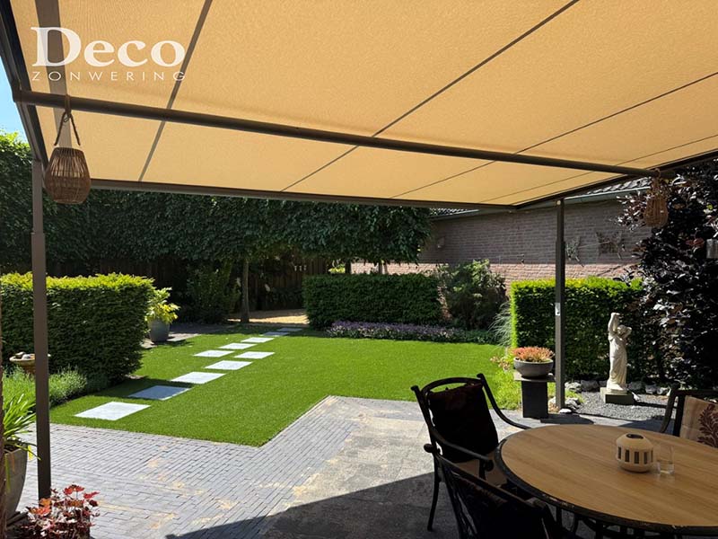 weinor-plaza-viva-overkapping-venhorst-terras-tuinset Aanzicht van een Weinor Plaza Viva overkapping van binnenuit, met een ronde houten tuintafel en stoelen op het terras, omgeven door een verzorgde tuin met hagen en beplanting.
