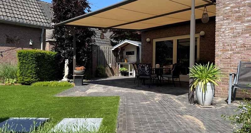 weinor-plaza-viva-terrasoverkapping-venhorst-zijaanzicht Weinor Plaza Viva doek overkapping in grijsbruin structuurlak met warm crème-taupe doek, geplaatst tegen een bakstenen woning in Venhorst, met zicht op de tuin en buitenmeubilair eronder.