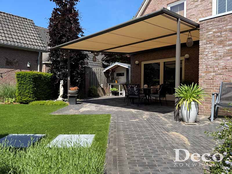 weinor-plaza-viva-terrasoverkapping-venhorst-zijaanzicht Weinor Plaza Viva doek overkapping in grijsbruin structuurlak met warm crème-taupe doek, geplaatst tegen een bakstenen woning in Venhorst, met zicht op de tuin en buitenmeubilair eronder.