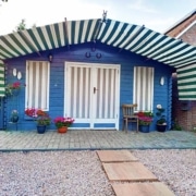 Tuinhuis met hergebruikt gestreept zonneschermdoek in groen en wit, gespannen over het dak en voor de deuren en ramen als duurzame zonwering.