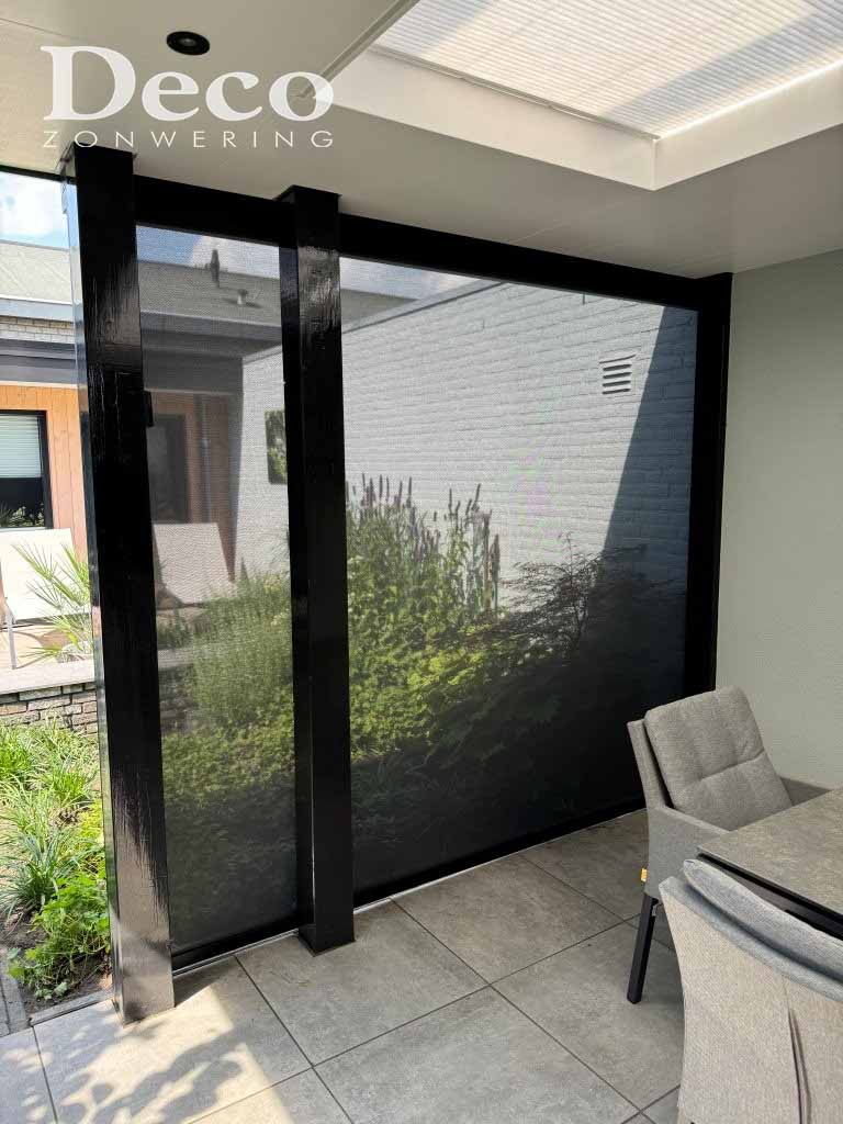 Windvaste Heroal solar screen zijkant overkapping Neergelaten windvaste Heroal solar screen aan de open zijkant van een overkapping in Heesch, met zicht op de tuin