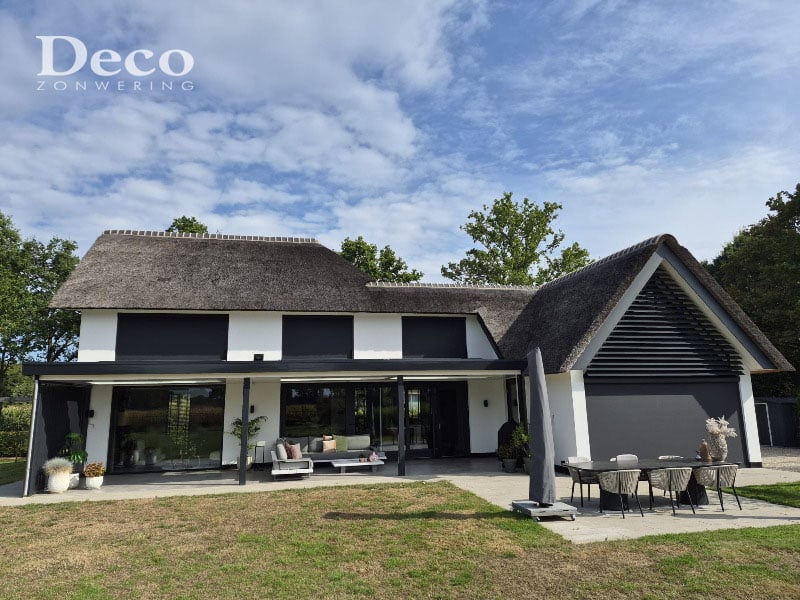 Achtergevel van een vrijstaande woning in Heesch met donkere solar screens, rieten dak en terrasoverkapping.